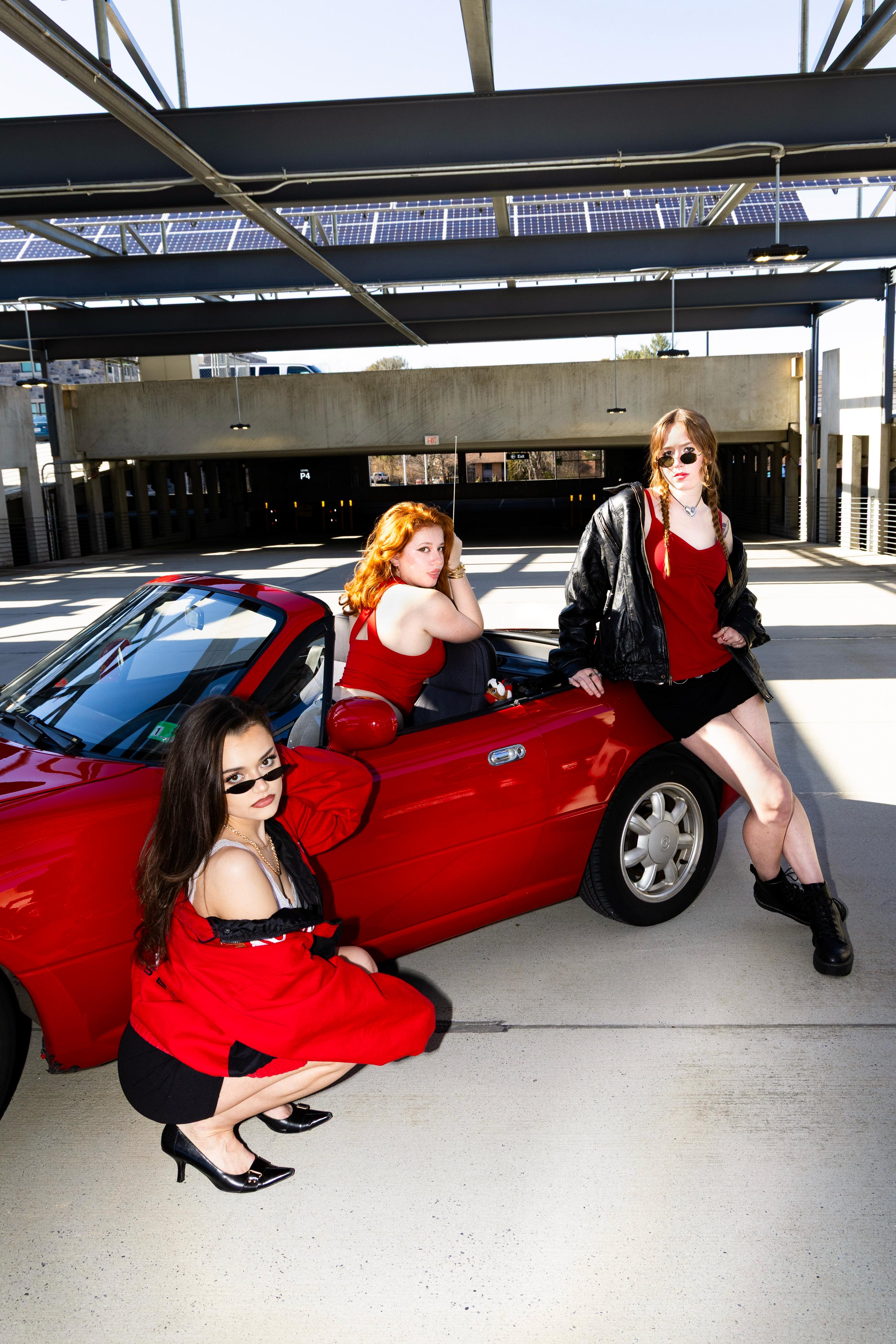 Three friends posing beside a red convertible